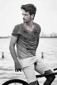 Young man looking away while sitting by sea