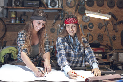 Smiling women drawing blueprint in workshop