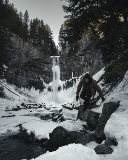 Man walking on snow covered land against waterfall