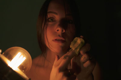 Portrait of woman holding fruit in darkroom