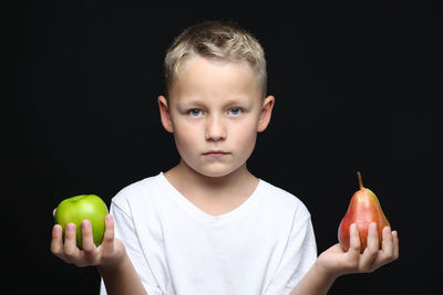 Boy holding apple against black background