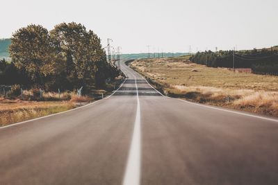 Empty road amidst trees against clear sky