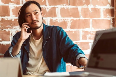 Man using mobile phone while sitting against wall