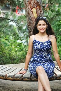Portrait of young woman smiling while sitting against trees