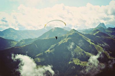 Person paragliding over mountains against sky