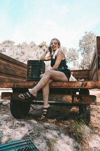 Portrait of woman sitting on bench against sky