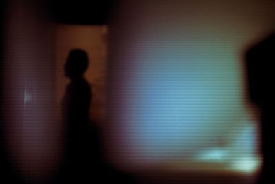 Defocused image of silhouette man standing on illuminated wall