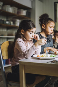 Girl having pasta for breakfast with female classmate in child care center