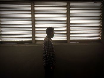 Side view of man wearing mask standing by window in darkroom