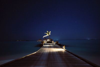 Pier over sea against clear blue sky at night