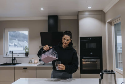Woman in kitchen pouring smoothie in glass