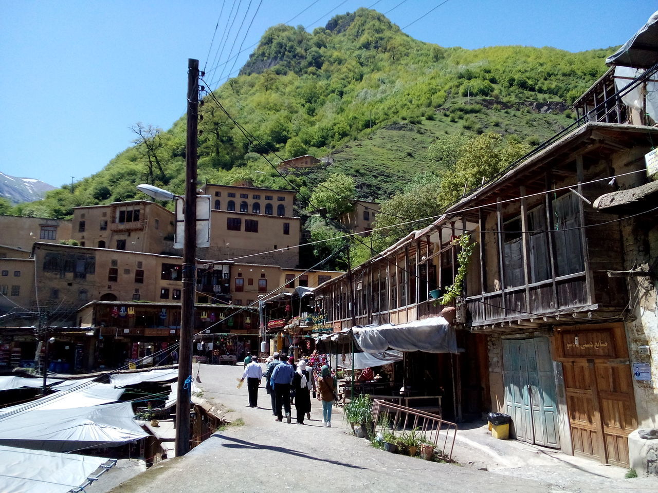 built structure, architecture, building exterior, mountain, building, sky, group of people, nature, residential district, day, city, transportation, tree, walking, sunlight, real people, incidental people, people, outdoors, clear sky