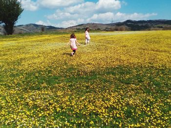 Girls walking amidst flowering plants on field during sunny day