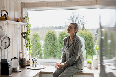 Mature woman sitting on kitchen counter at home