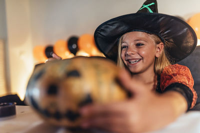 Smiling girl in costume looking away by pumpkin on table