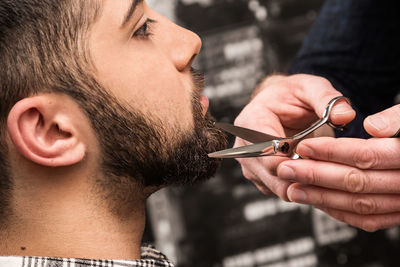 Cropped hands of barber trimming beards of man