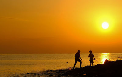 Silhouette men on beach against sky during sunset