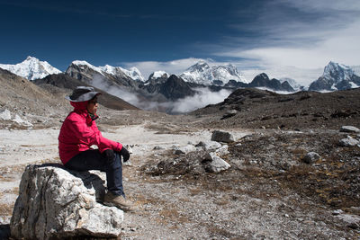 Side view of mid adult woman sitting on rock against sky during sunny day