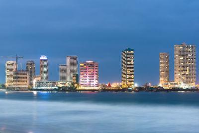 Sea by illuminated buildings against blue sky