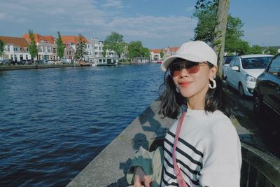 Portrait of young woman standing against river