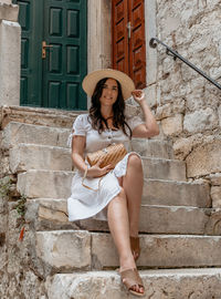 Lifestyle photo of beautiful young woman wearing white dress, sitting on stone stairs