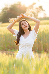 Young beautiful woman holding cut dried barley over her head while standing in the barley field