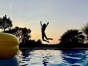 Silhouette man jumping in swimming pool against sky
