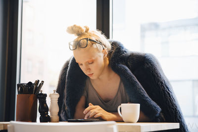 Young transgender customer using smart phone while sitting at table in cafe