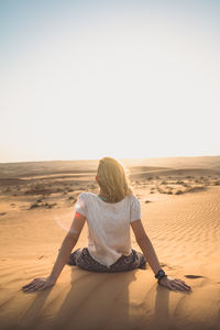 Rear view of woman sitting on sand at beach