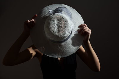 Woman holding hat against while standing against black background