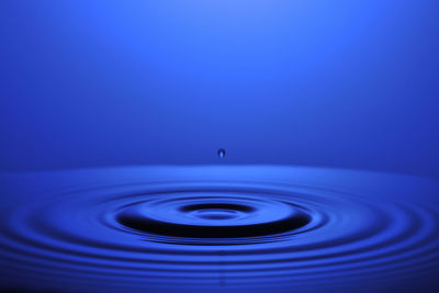 Close-up of drop falling on water against blue background