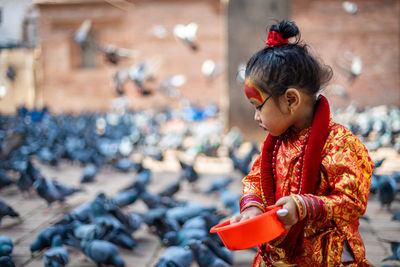 Girl wearing traditional clothing feeding crows