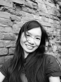 Portrait of smiling young woman standing against brick wall