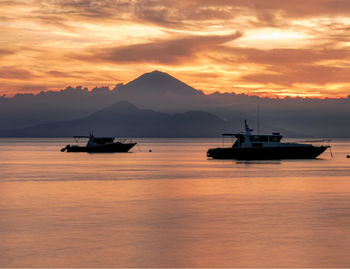 Silhouette boats in sea against orange sky