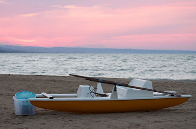 Boat moored on beach against sky during sunset