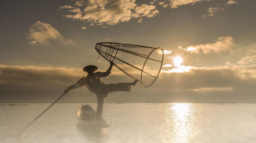 Fisherman on lake against sky during sunset