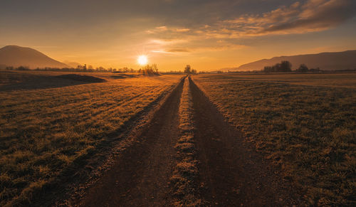 Road amidst field against sky during sunset