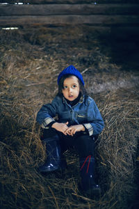 Village boy a child in boots is sitting
on the hay in a barn in warm clothes and a blue hat