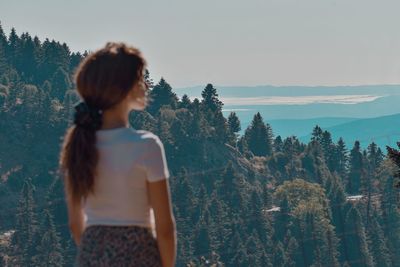 Rear view of woman standing by forest against sky