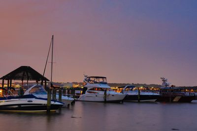Boats moored in harbor at sunset