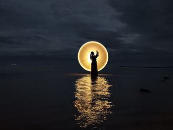 Illuminated lamp on sea against sky during sunset