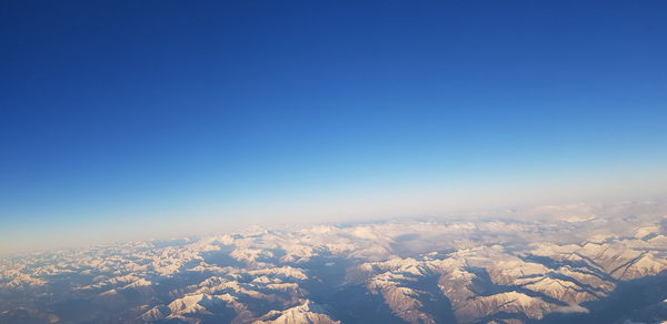 Aerial view of snowcapped mountains against clear blue sky