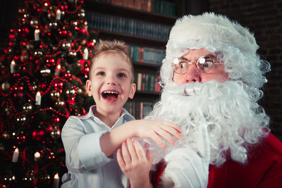 Smiling boy with santa clause against christmas tree at home