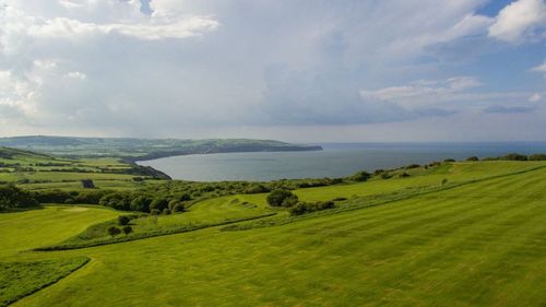 Scenic view of green landscape and sea against sky