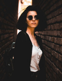 Portrait of young woman wearing sunglasses standing against wall