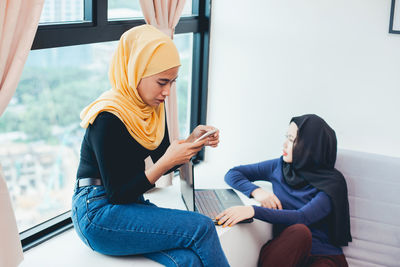 Side view of women sitting on window