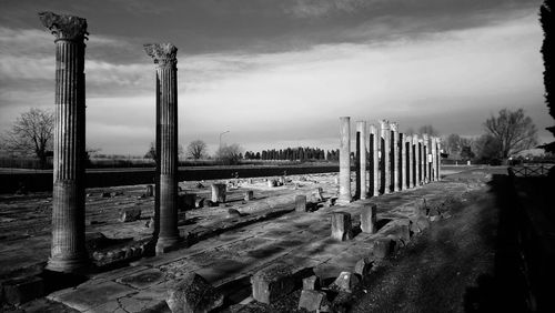 Old architectural columns at cemetery against sky