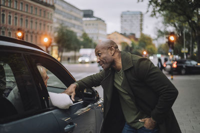 Bald mature man talking to woman sitting in car