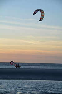 Silhouette people kiteboarding in sea against sky