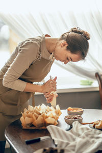 Young woman applies cream to cupcakes in craft paper. food delivery. birthday package. chef bakes